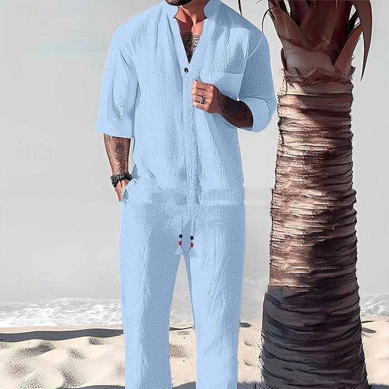 Person wearing a light blue jumpsuit standing on a beach with a palm tree.