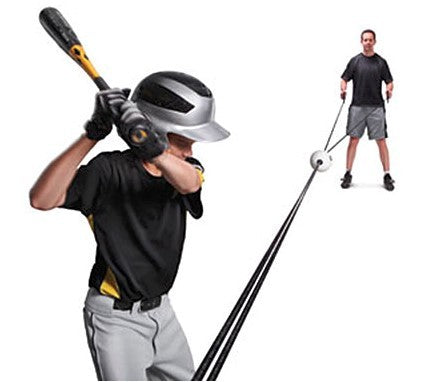 Person holding a baseball bat and wearing a helmet, with another person in the background using a pitching machine.