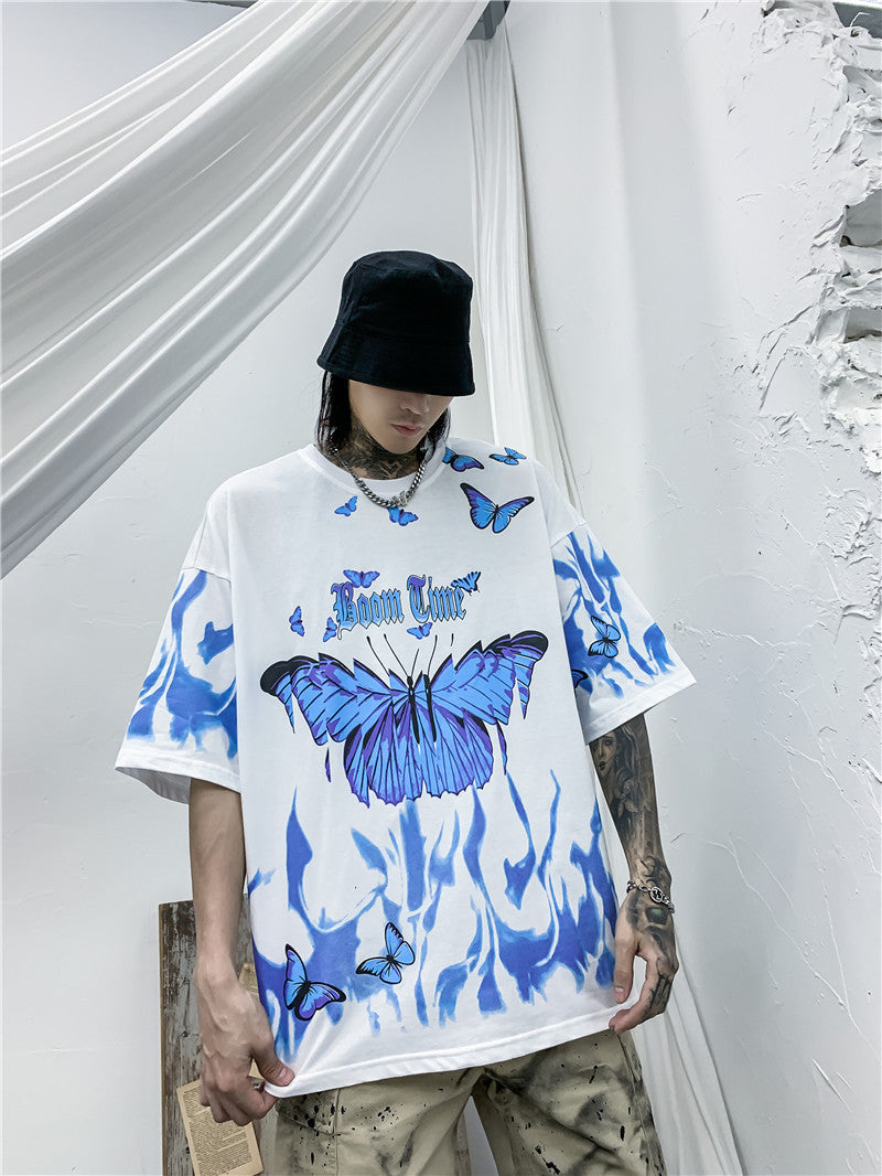 Person wearing a white t-shirt with blue butterfly designs against a white curtain background
