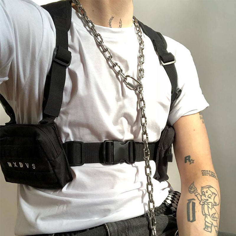 Person wearing a white t-shirt, black backpack, and carrying a chain, with tattoos visible on arms.