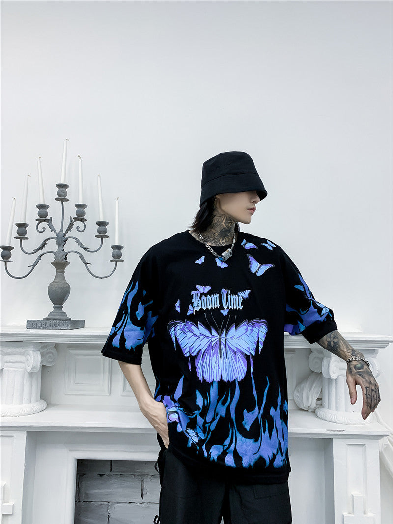 Person wearing a black and blue tie-dye shirt with 'Boom Clap' text, standing in a minimalistic room.