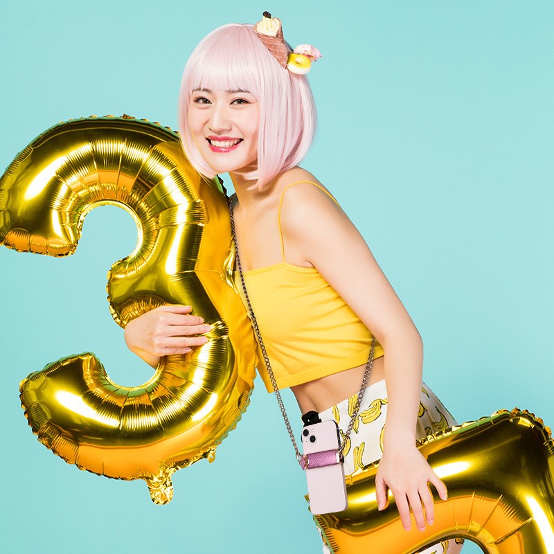 Person with pink hair holding gold number 3 balloons against a blue background