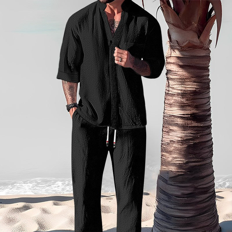 Person wearing a black outfit standing on a beach with a palm tree.