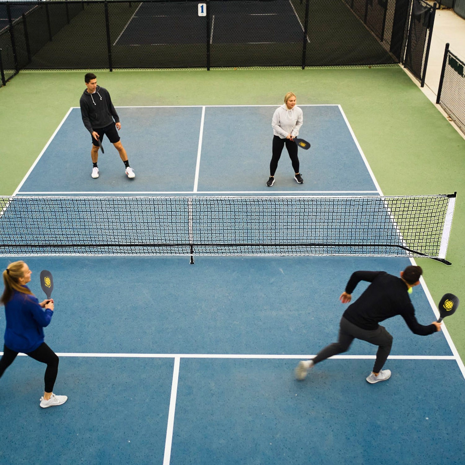 Four people playing paddle tennis on a blue court with a net.