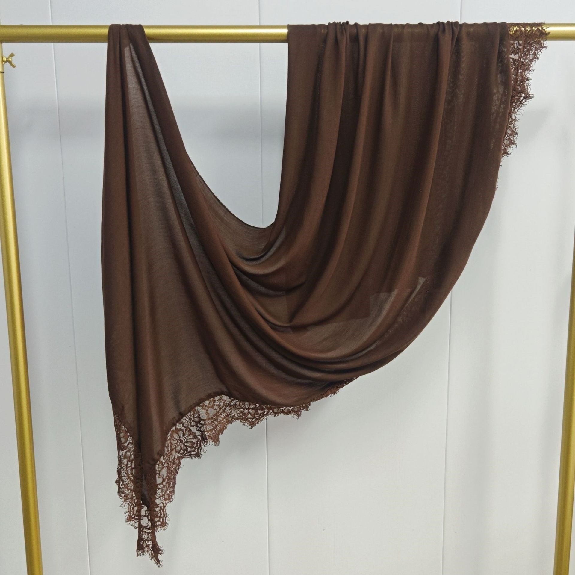 Brown scarf with lace trim draped over a gold rod against a white background
