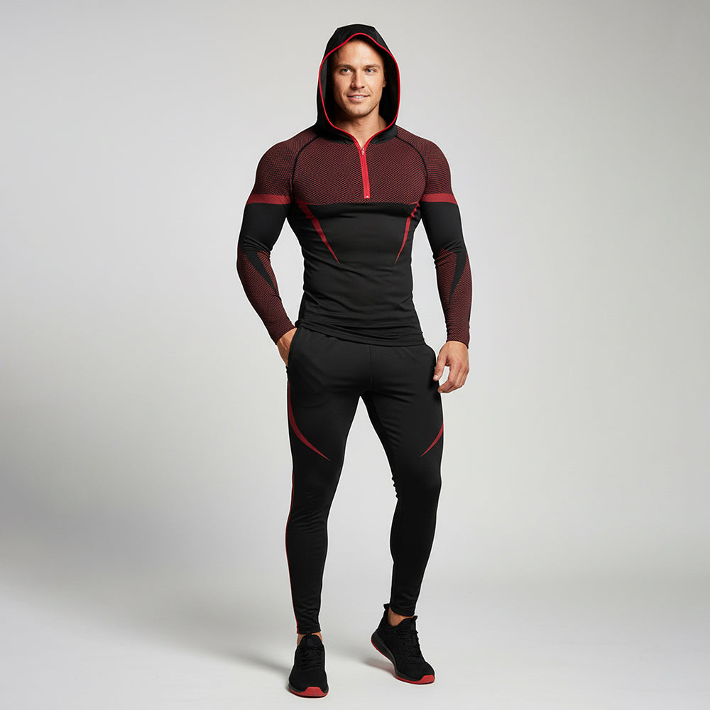 A man modeling a black and dark red athletic half-zip hoodie and matching black leggings with red accents, standing against a light gray studio background.