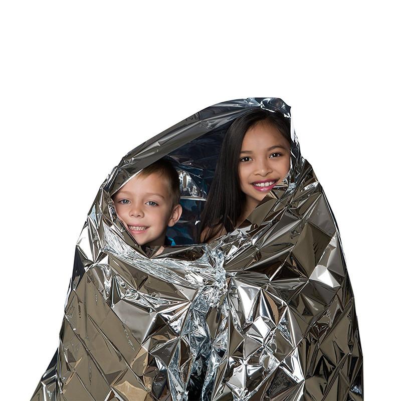 Two children peeking out from a silver mylar blanket on a white background