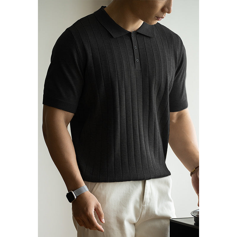 Person wearing a black ribbed polo shirt and white pants against a neutral background