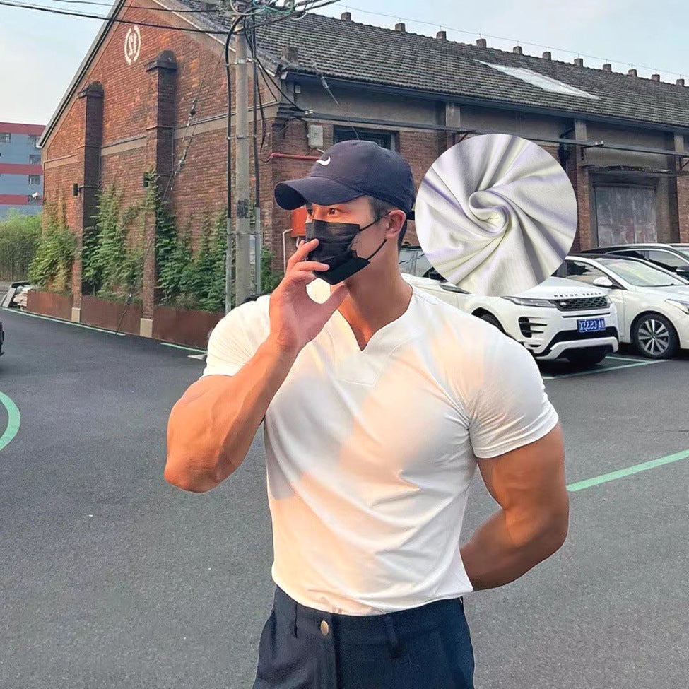Man in a white t-shirt and cap standing on a street with cars and buildings in the background