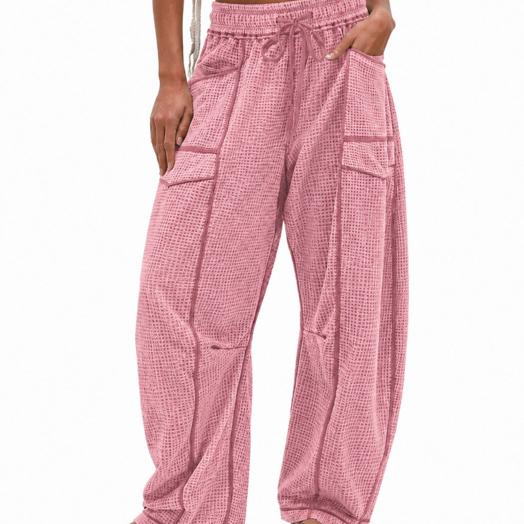 Pink waffle-knit harem pants with a drawstring waist, side pockets, and large front patch pockets, shown on a model against a white background.