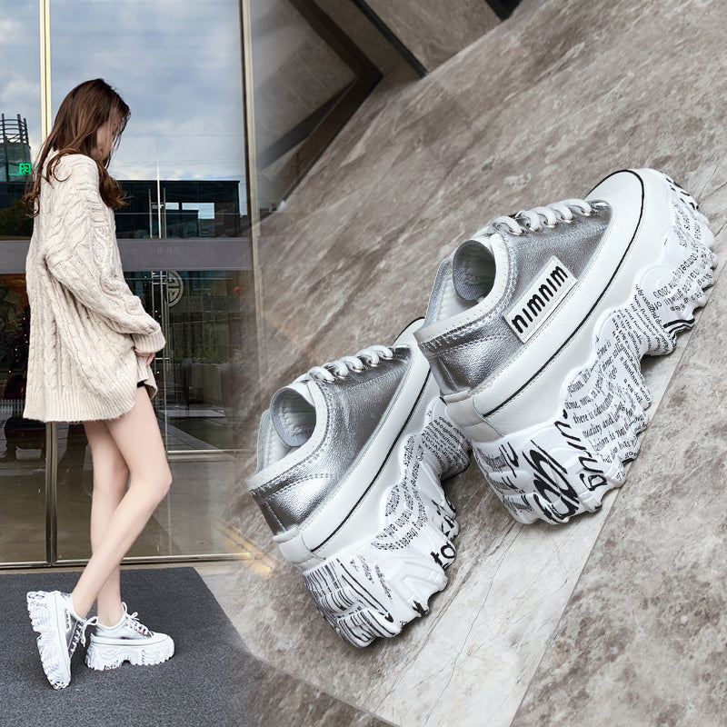 Silver sneakers with text design on a concrete floor, with a person wearing them in the background.