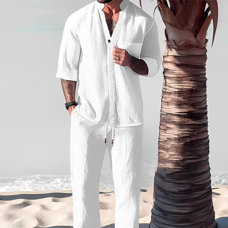 Man in white linen outfit standing on a beach with palm tree