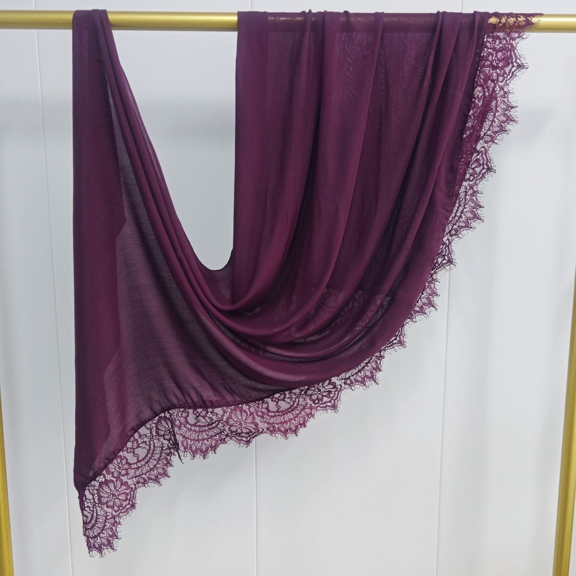 Purple scarf with lace edge on a gold rod against a white background