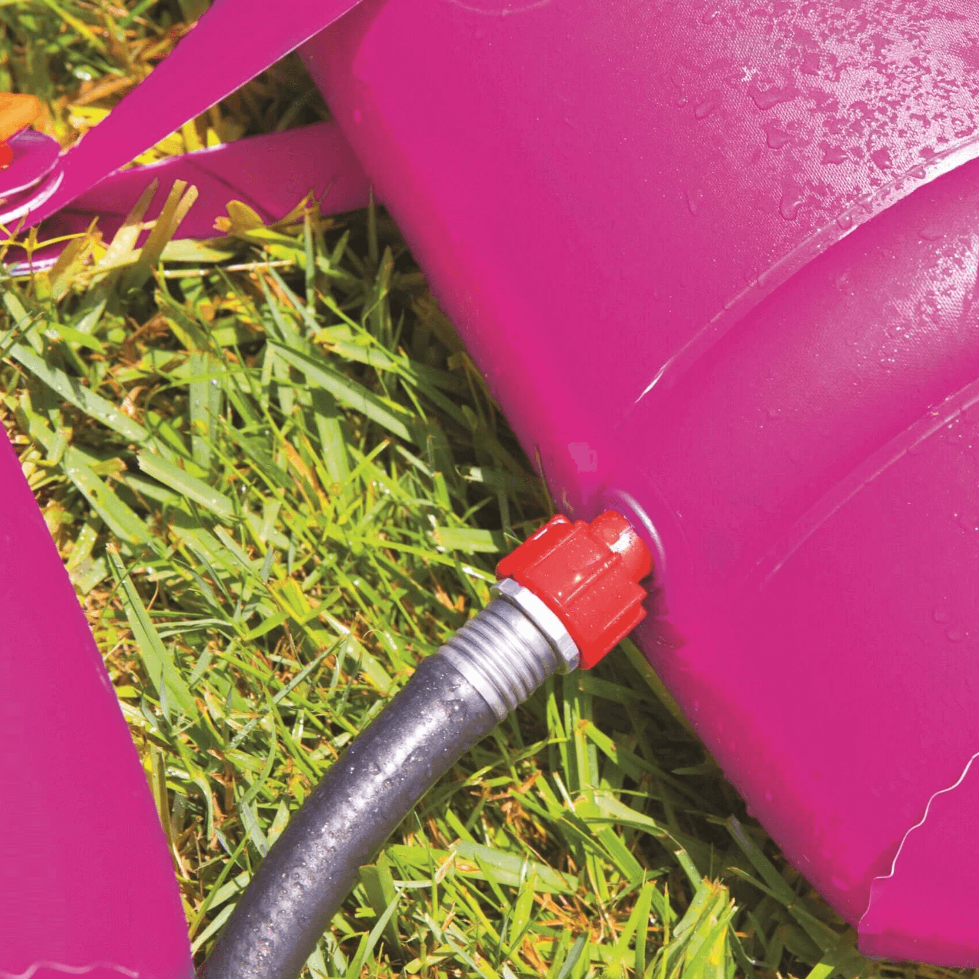 Pink with a red valve and black hose on grass