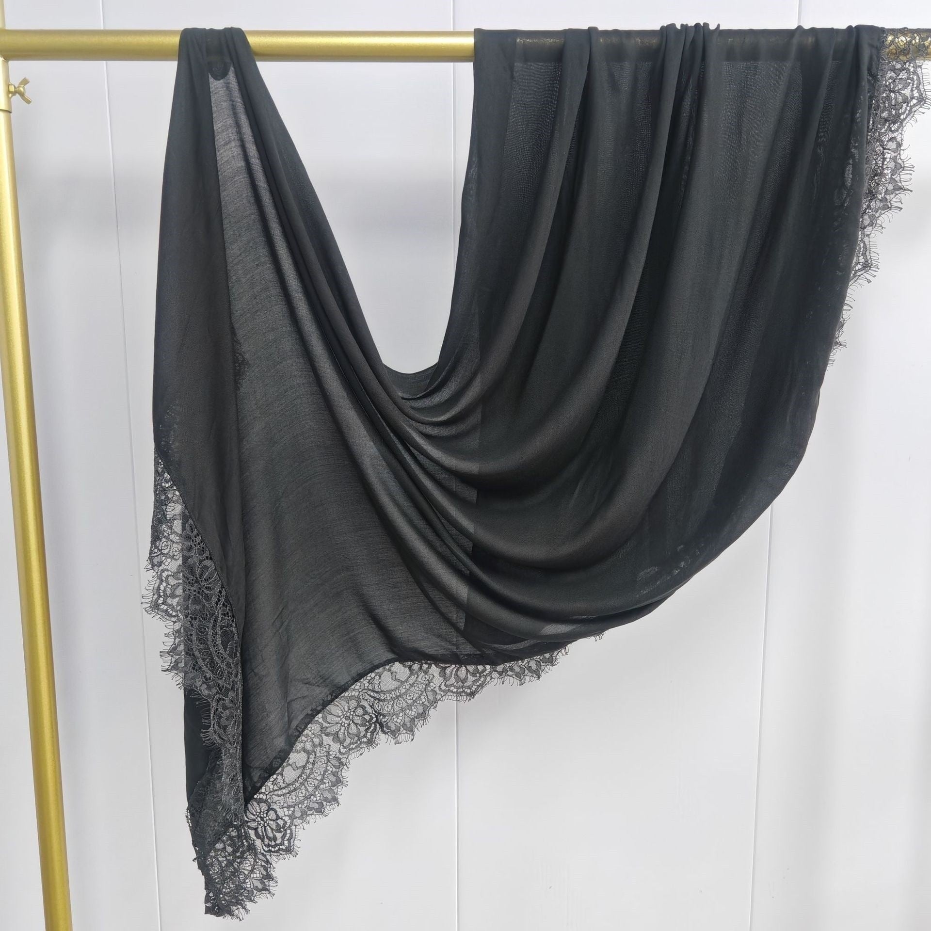 Black scarf with lace trim draped over a gold rod against a white background