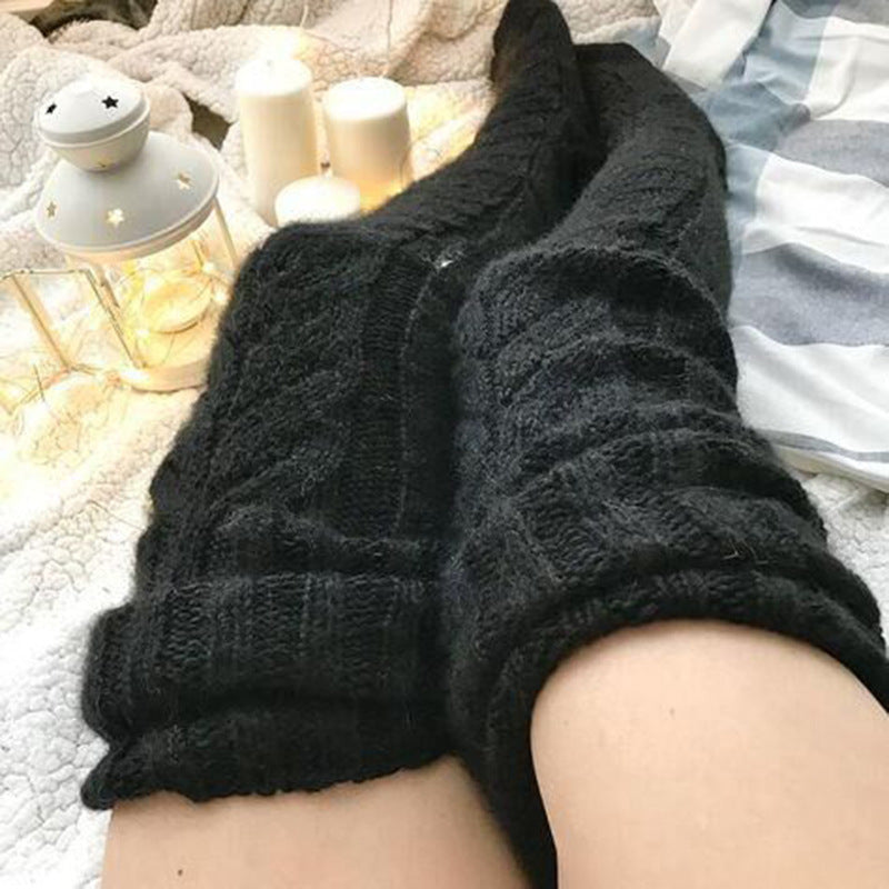 Black cable knit socks being worn on a soft surface with candles in the background