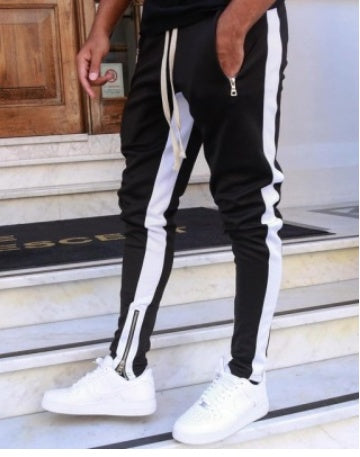 Person wearing black and white track pants with white sneakers on a staircase.