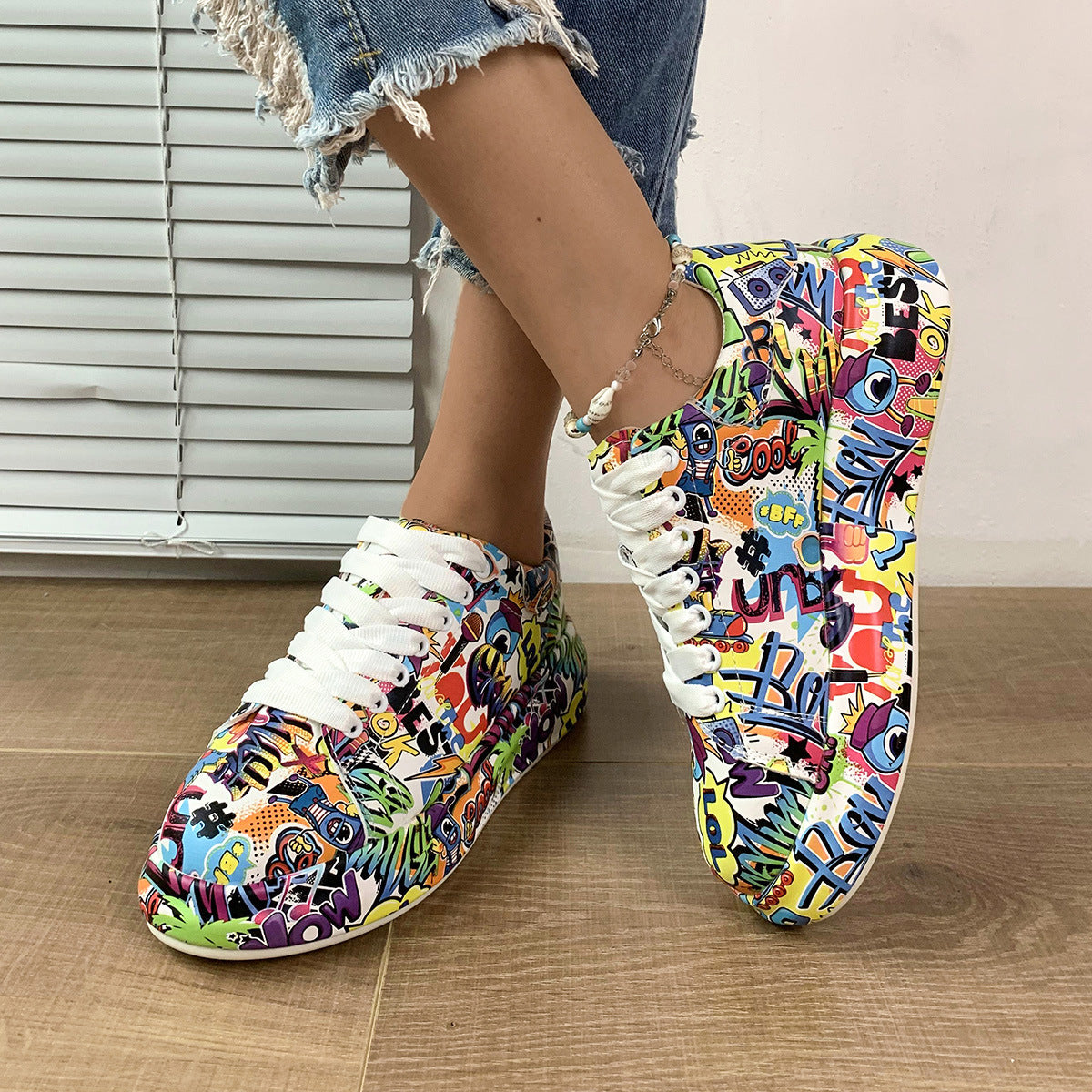 Colorful graffiti-style sneakers with white laces worn by a person on a wooden floor.