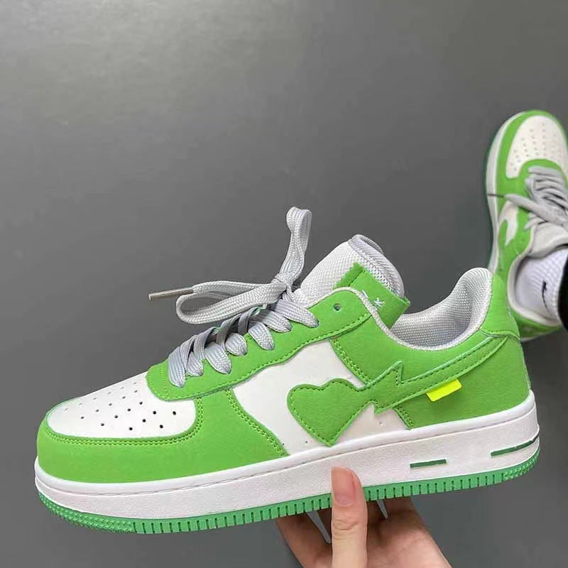 Green and white sneaker with a heart design held by a hand against a gray background