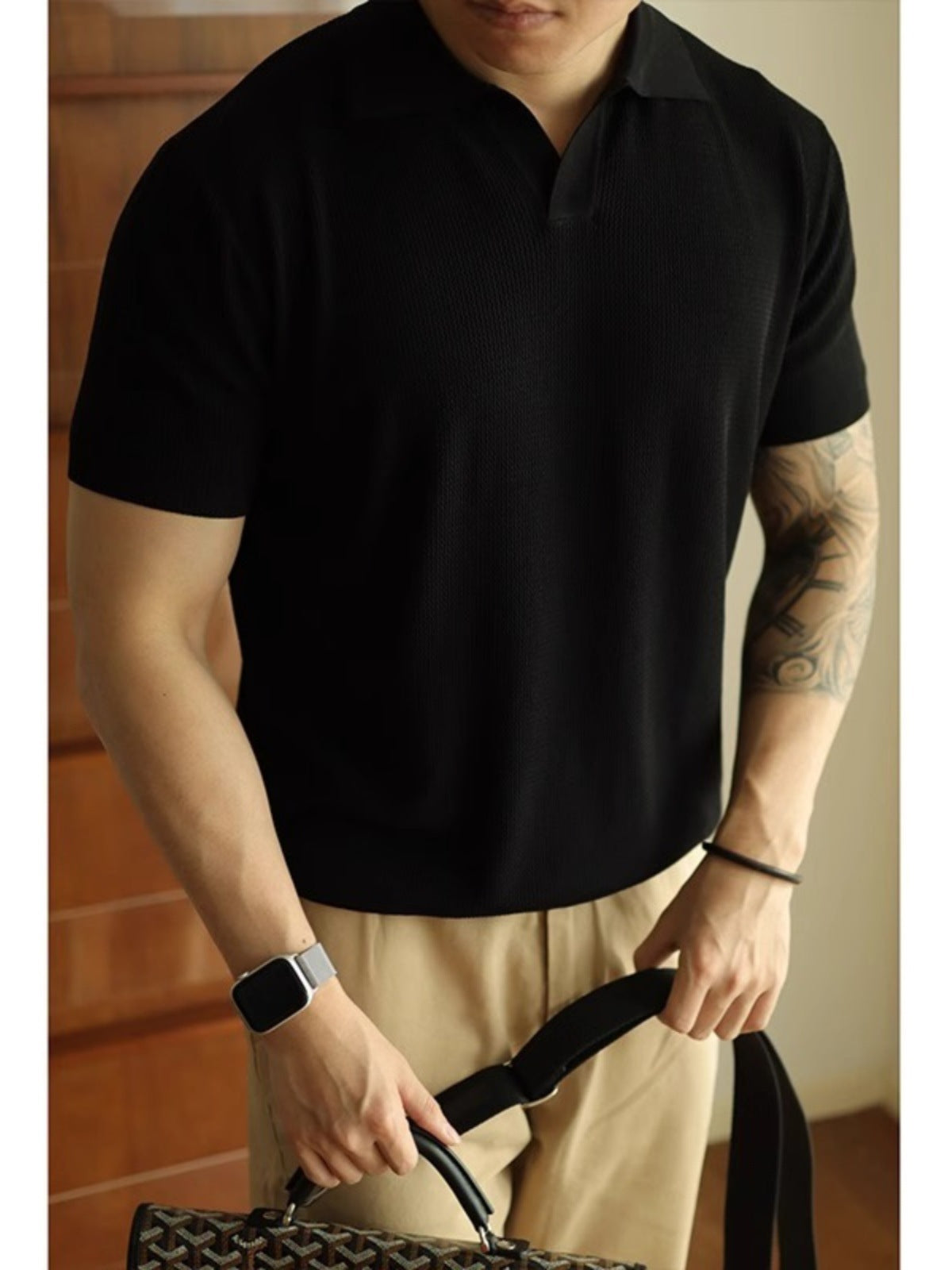 Person wearing a black polo shirt and beige pants, holding a bag.