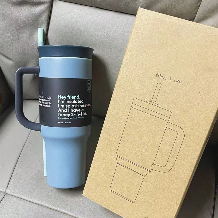 Blue-gray 40 oz travel tumbler with dark handle, lid and straw beside a cardboard product box.