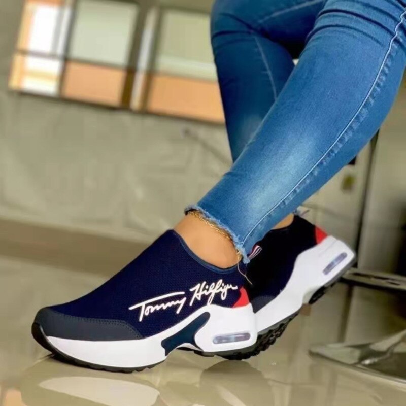 Navy and white slip-on shoes with red accents worn with blue jeans indoors.