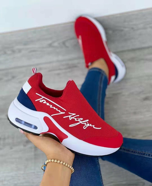 Red and blue Tommy Hilfiger sneakers worn by a person sitting on a wooden floor.