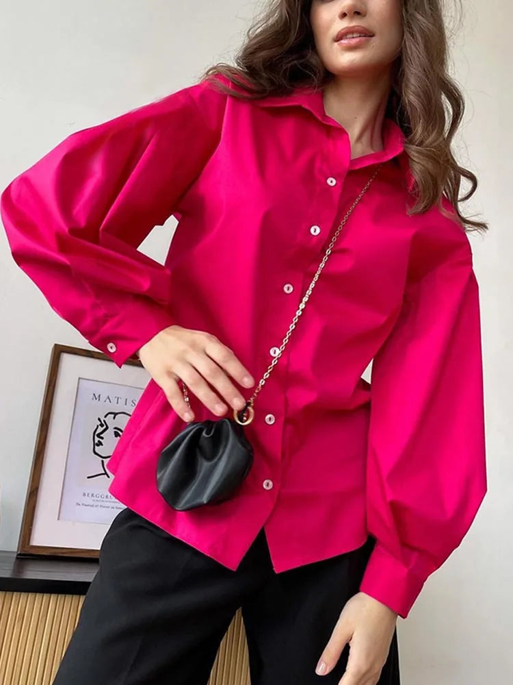 Woman wearing a bright pink shirt holding a black handbag indoors.