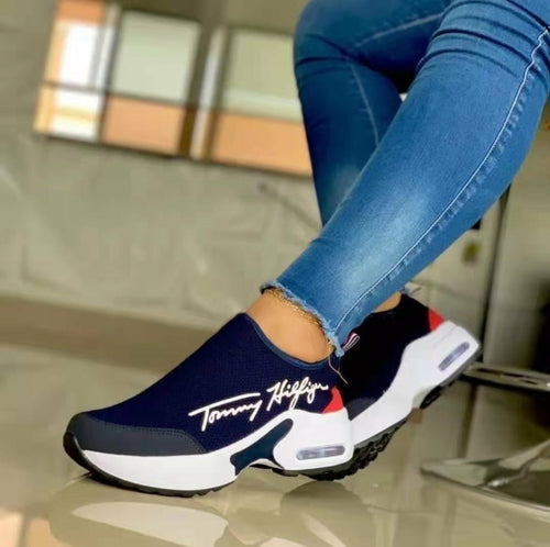 Navy slip-on sneakers with white sole and red accents worn with blue jeans indoors.