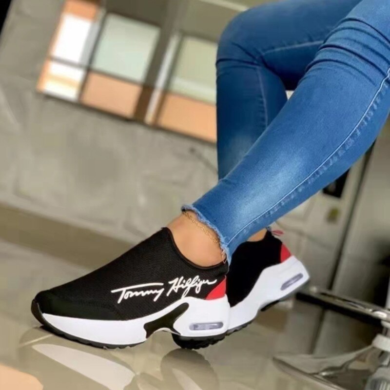 Black and white sneakers with red accents worn with blue jeans in an indoor setting