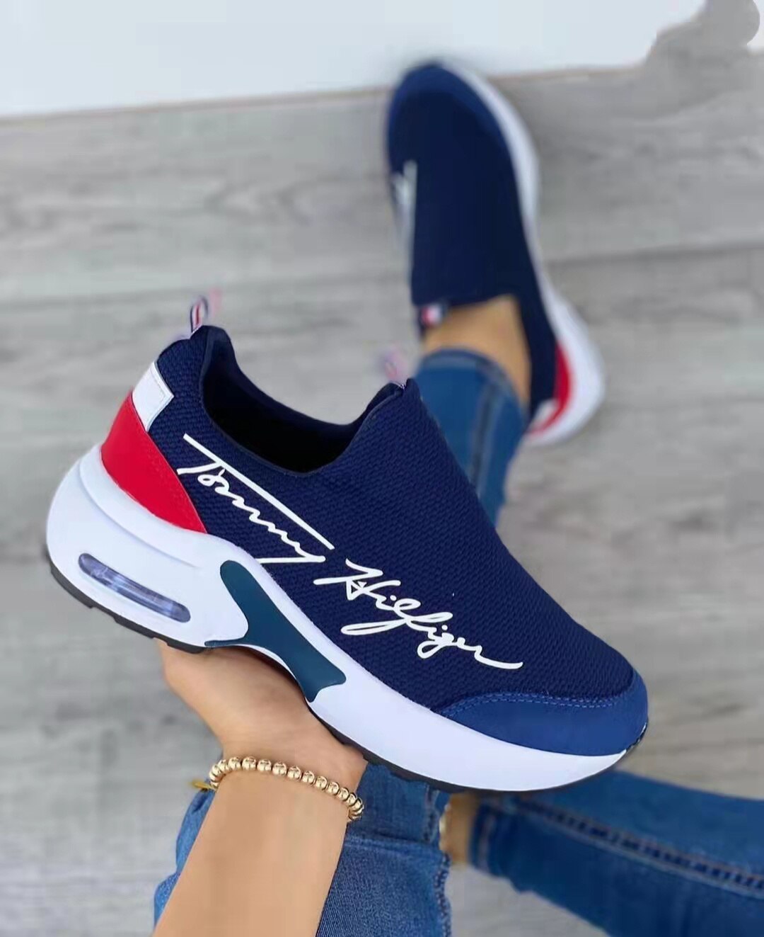 Navy slip-on sneaker with red and white accents held by a person wearing blue jeans.