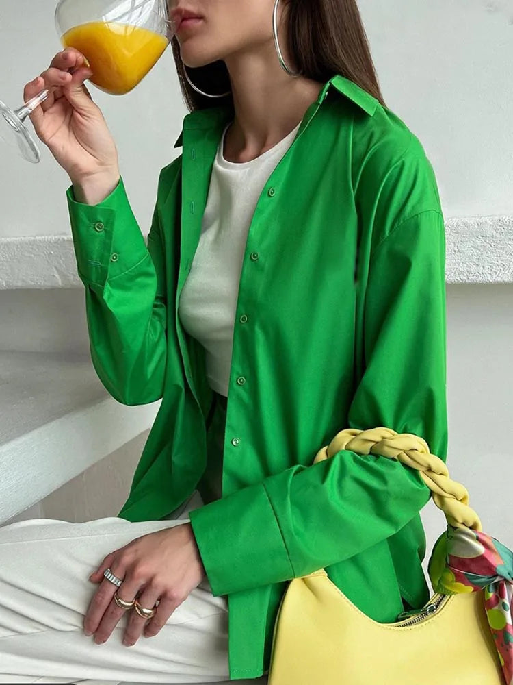 Woman in a green jacket holding a glass of orange juice and a colorful bag.