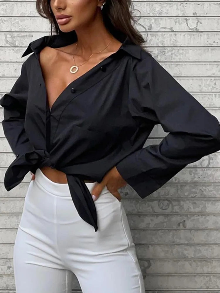 Woman wearing a black tied blouse and white pants against a gray wooden background