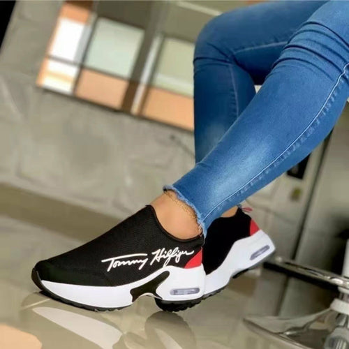 Black and white sneakers with red accents worn by a person in blue jeans, on a reflective surface.