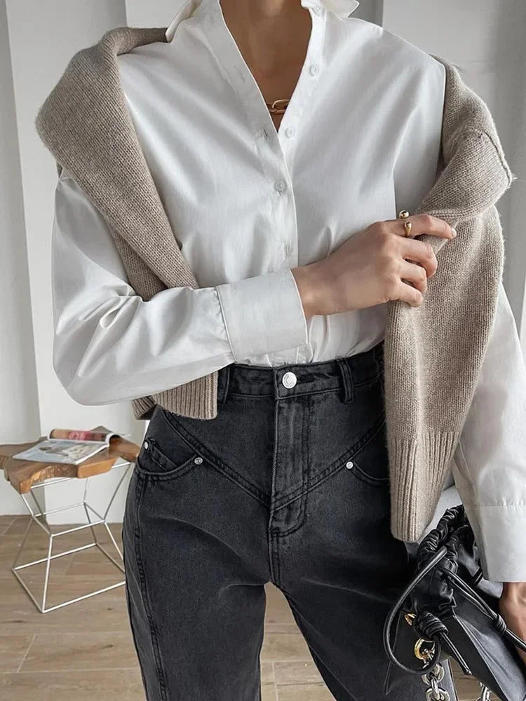 Person wearing a white shirt, beige cardigan, and black pants in an indoor setting.