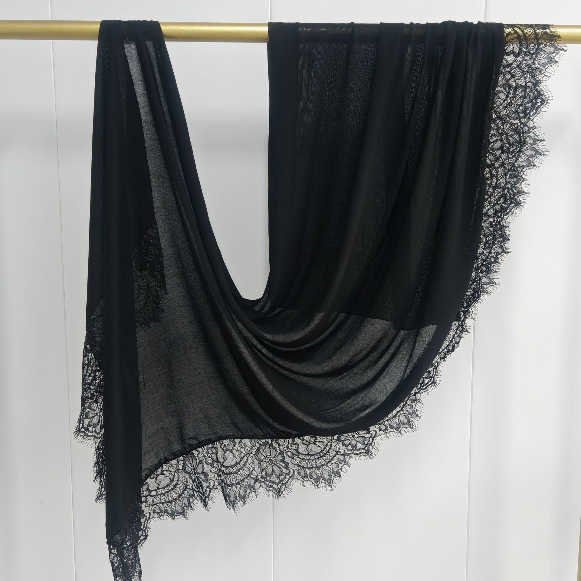 Black scarf with lace trim draped over a gold rod on a white background
