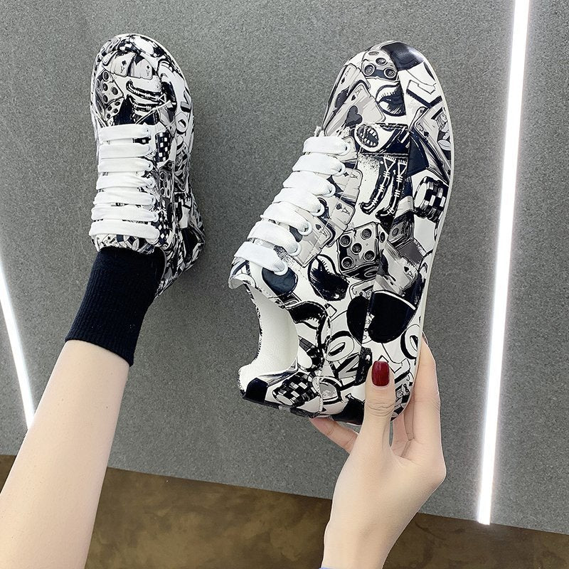 White sneakers with black and gray abstract pattern held by a person against a neutral background