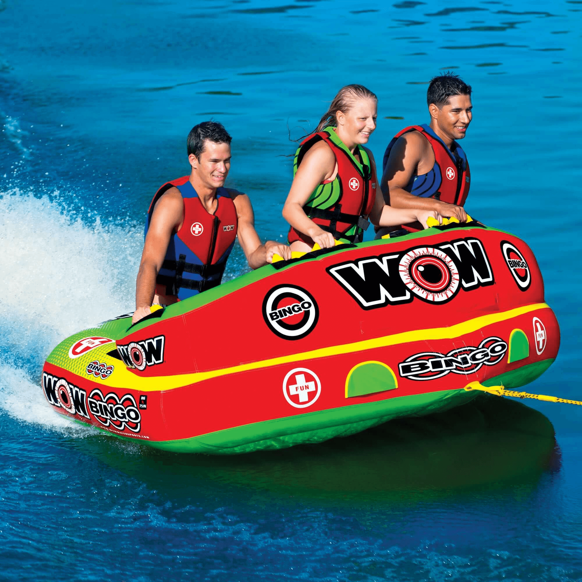 Three people on a red and green inflatable tube with 'WOW' branding in the water.