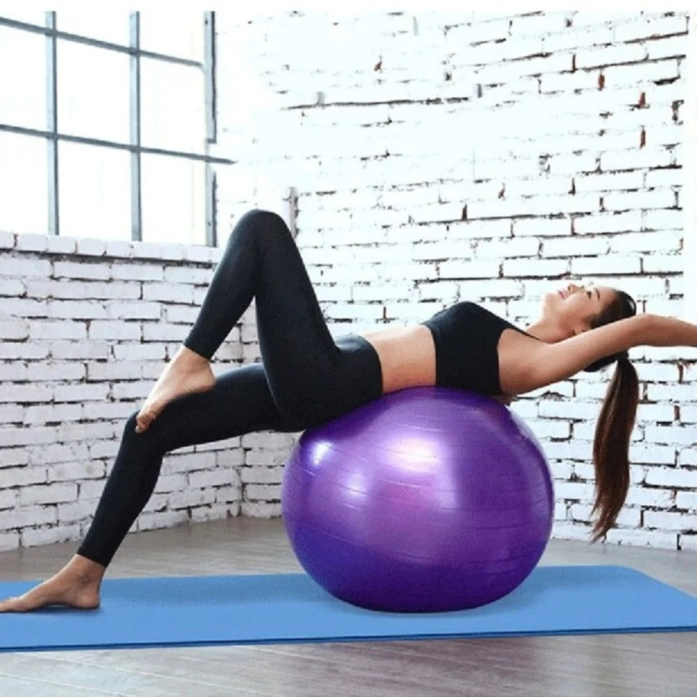Woman exercising on a purple stability ball against a white brick wall.