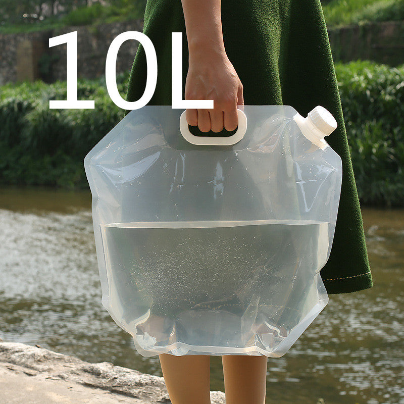 Person holding a transparent water container with a green coat, standing by a body of water.
