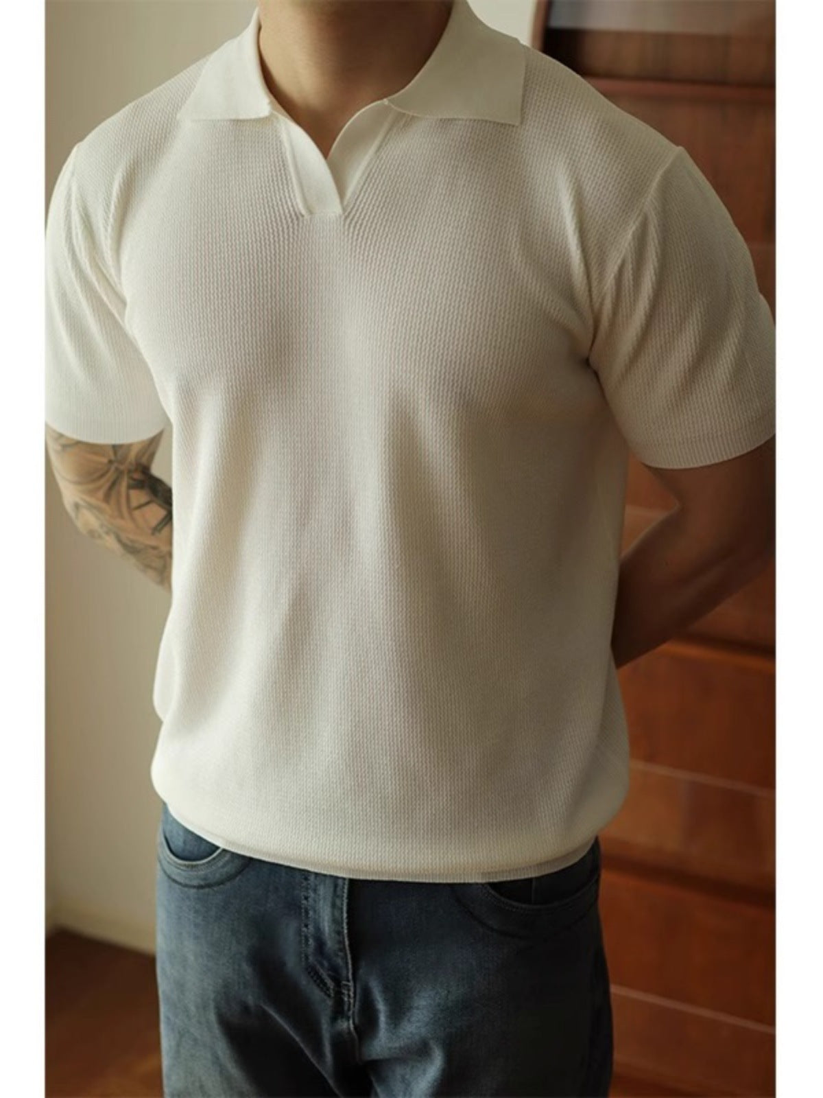 Person wearing a white polo shirt and dark jeans indoors.