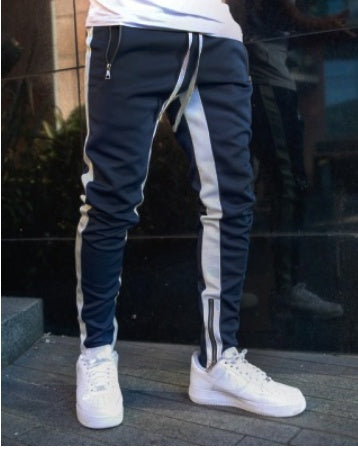 Person wearing navy jogger pants with white stripes and white sneakers in front of a dark background.