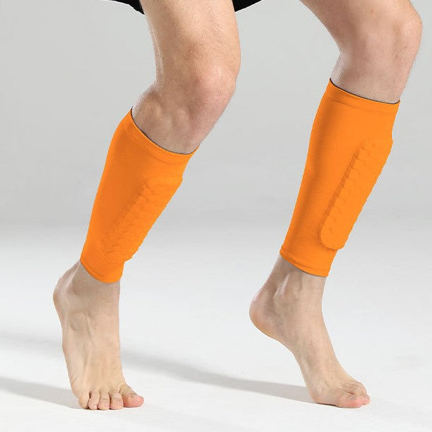 Bright orange athletic shin and calf sleeves worn on both legs, shown on a model against a light gray studio background.
