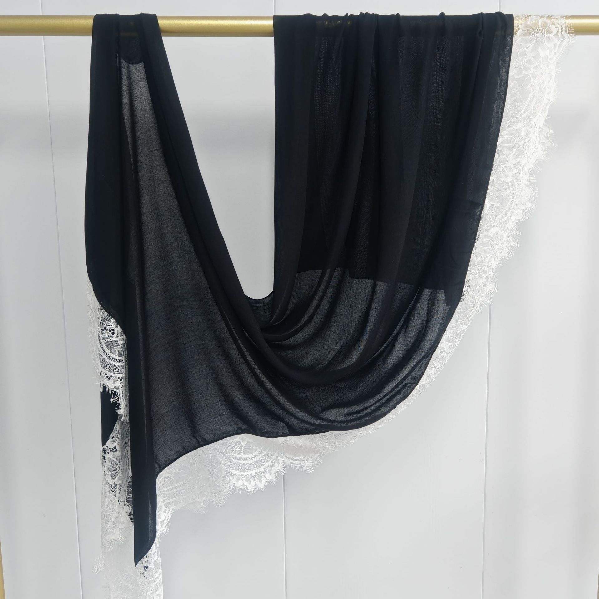 Black scarf draped over a gold rod against a white lace curtain background