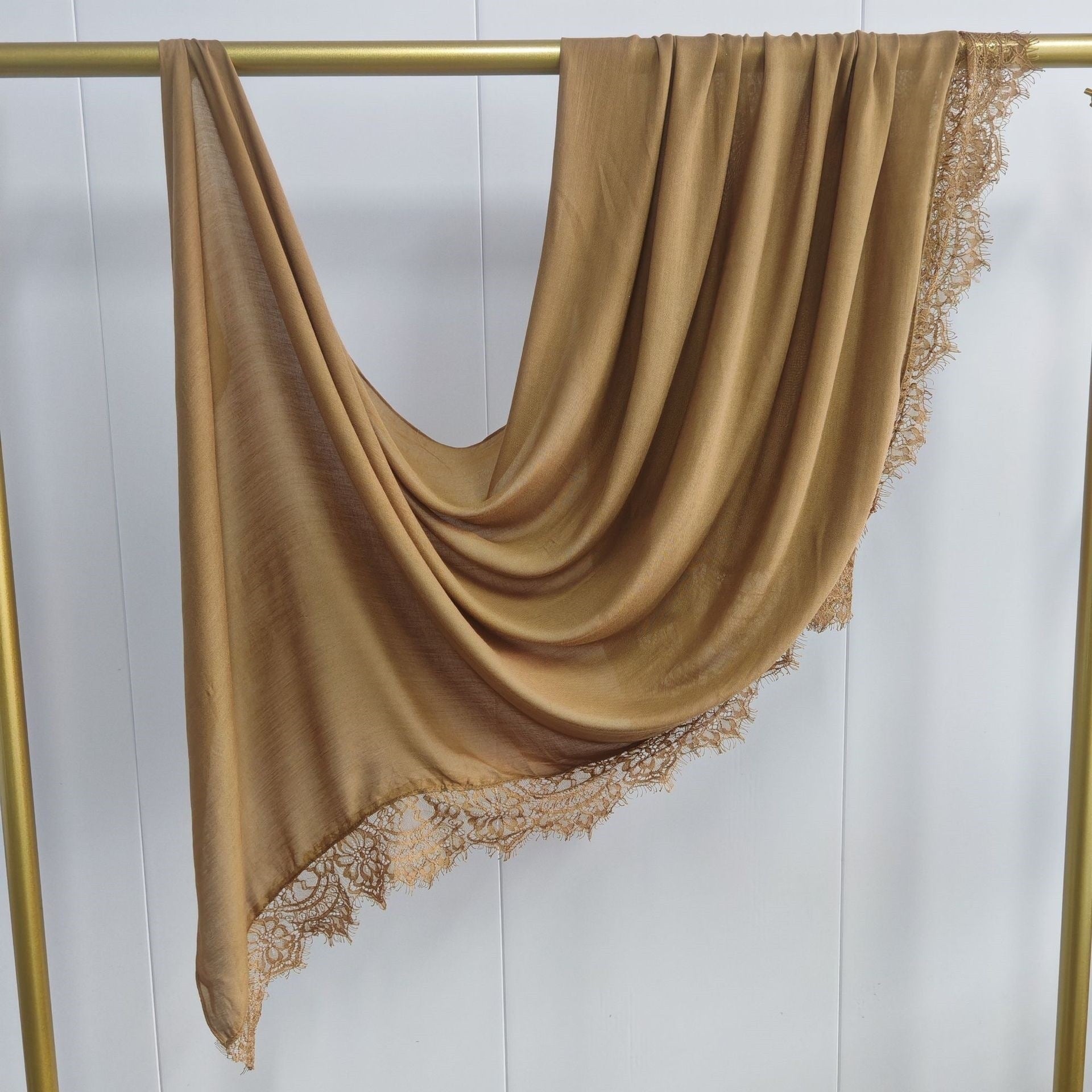 Brown scarf with lace trim draped over a gold rod against a white background