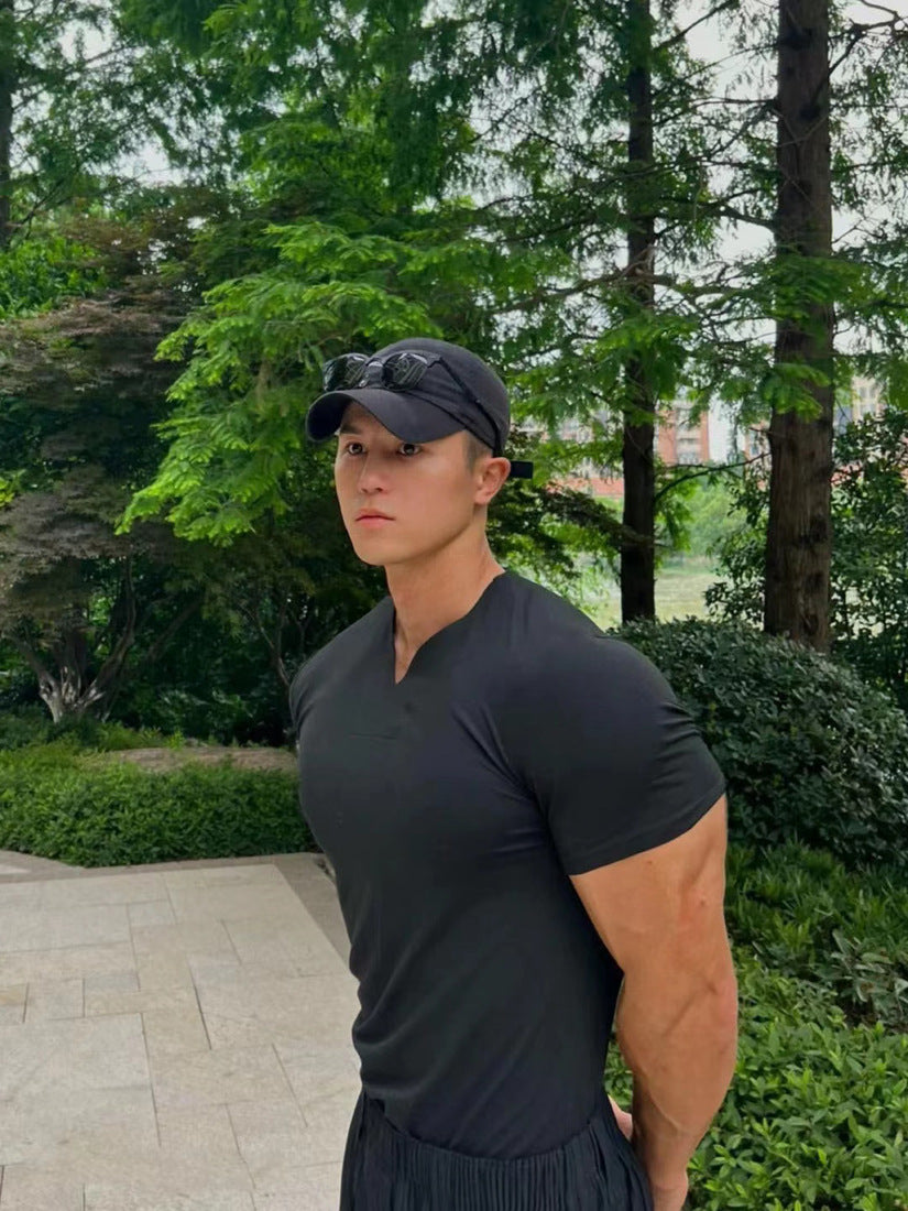 Person wearing a black cap and black shirt outdoors with greenery in the background