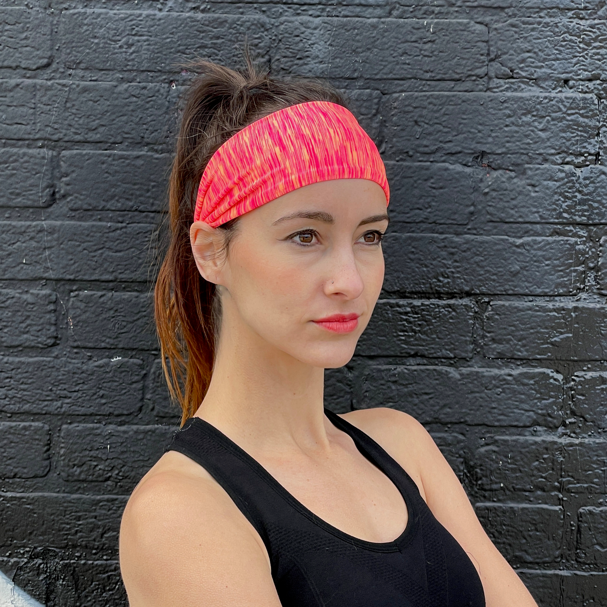 Woman wearing a pink headband against a black brick wall