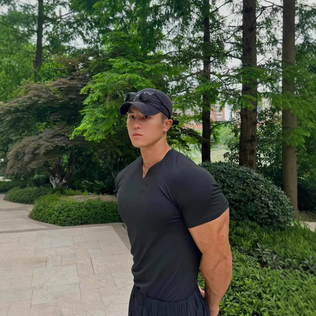 Person wearing a black cap and t-shirt standing outdoors with greenery in the background