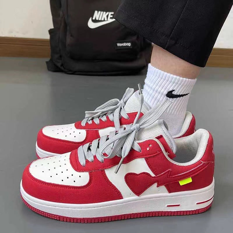 Red and white sneakers with a heart design worn by a person, with a black Nike backpack in the background.