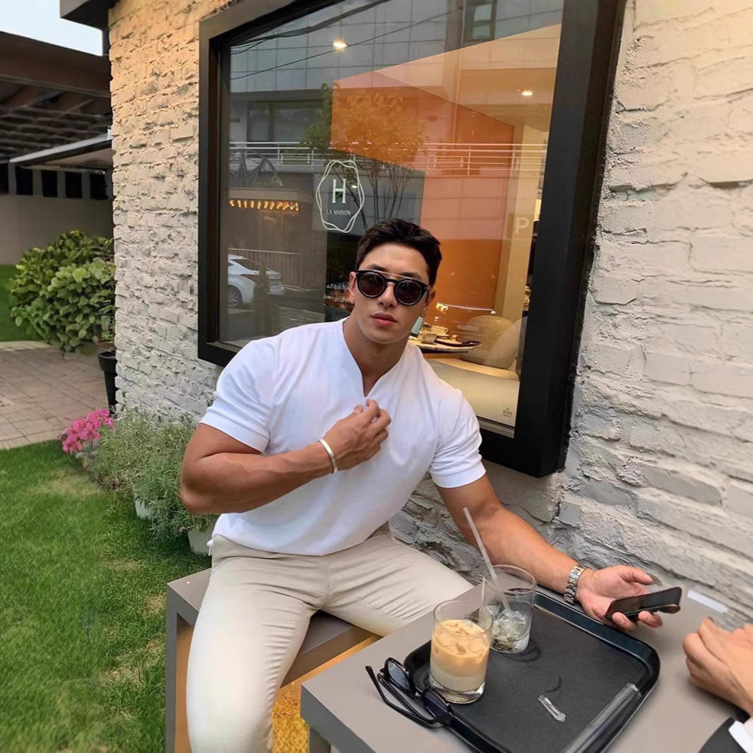 Man sitting outdoors with a drink and phone, wearing sunglasses and a white shirt.